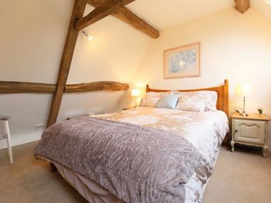 A bedroom with a wooden bed frame bedside tables with lamps decorative beams on the walls and a framed picture at Pike Cottage in Stow-On-The-Wold