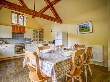 A kitchen with wooden chairs and a table with tablecloth and dishes at Little Barn in Ascott near Chipping Norton