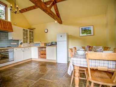 A kitchen with white cabinets a dining table set with dishes and glasses and wooden chairs at Little Barn in Ascott near Chipping Norton