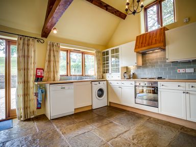 A kitchen with white cabinets stone floor dishwasher washing machine and oven at Little Barn in Ascott near Chipping Norton