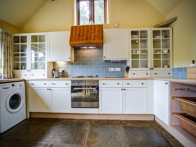 A kitchen with white cabinets a stove a washing machine and a window at Little Barn in Ascott near Chipping Norton