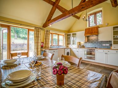A kitchen with wooden beams a dining table set with plates glasses and flowers at Little Barn in Ascott near Chipping Norton