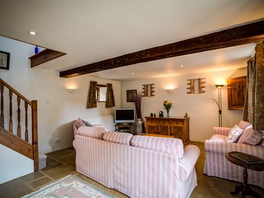A living room with striped sofas wooden furniture a television and a staircase at Little Barn in Ascott near Chipping Norton