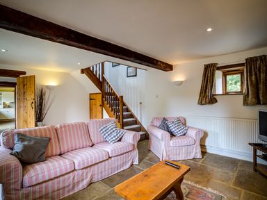 A living room with striped sofas a wooden coffee table stairs and a television at Little Barn in Ascott near Chipping Norton