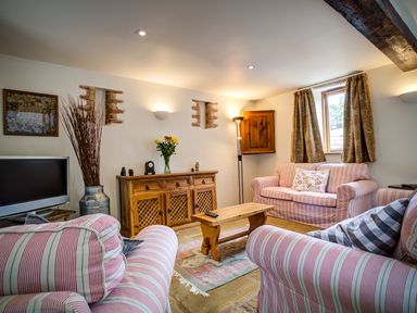 A living room with striped sofas a wooden coffee table a wooden cabinet flowers and a television at Little Barn in Ascott near Chipping Norton