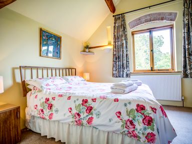A bedroom with a double bed with floral bedding a window with curtains and a framed picture on the wall at Little Barn in Ascott near Chipping Norton