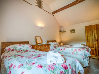A bedroom with two single beds with floral bedding a wooden dresser and wardrobe at Little Barn in Ascott near Chipping Norton
