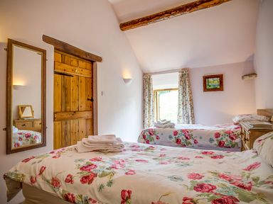 A bedroom with two beds with floral bedding a wooden door a mirror and floral curtains at Little Barn in Ascott near Chipping Norton