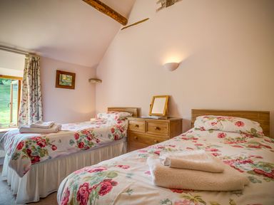 A bedroom with two single beds with floral bedding a wooden chest of drawers and a window at Little Barn in Ascott near Chipping Norton