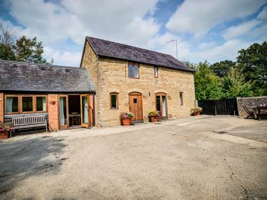 Exterior view of a stone and brick house with wooden doors and windows and flower pots at Little Barn in Ascott near Chipping Norton
