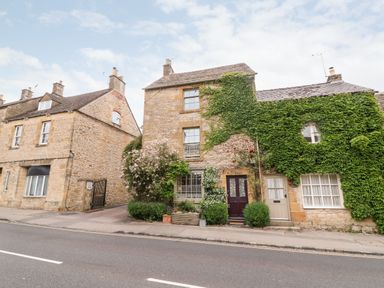 A stone house with greenery on the facade and two doors next to a street at Benfield in Stow-on-the-Wold