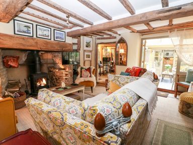 A living room with patterned sofas a wood burning stove and exposed wooden beams at Benfield in Stow-on-the-Wold