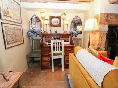 A small room with a wooden roll-top desk and chair a mustard sofa with cushions a floor lamp maps on the wall and decorative mirrors with flowers Benfield Stow-on-the-Wold
