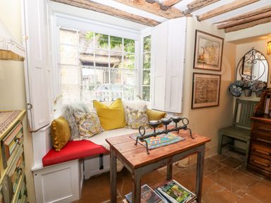 A corner seating area with cushions and a wooden table displaying a candle holder at Benfield in Stow-on-the-Wold