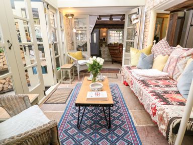 A room with wicker chairs a wooden coffee table with flowers and a book and a sofa with patterned cushions at Benfield in Stow-on-the-Wold