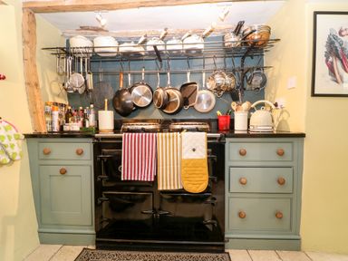 A kitchen stove with hanging pots pans and cooking utensils above and green cabinets below at Benfield in Stow-on-the-Wold