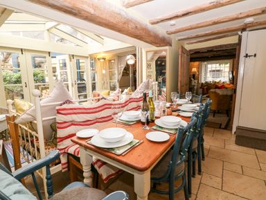 A dining area with a wooden table set with white plates and glasses next to a seating area with cushions at Benfield in Stow-on-the-Wold