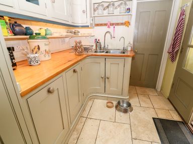 A kitchen with wooden countertops a double sink cabinets and pet food bowls on the tiled floor at Benfield in Stow-on-the-Wold