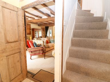 Carpeted stairs next to an open wooden door leading to a living room with a sofa and armchair at Benfield in Stow-on-the-Wold
