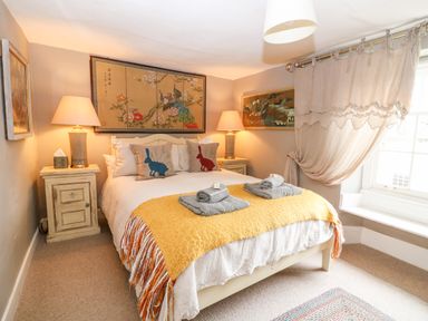 A bedroom with a bed covered with a yellow blanket and two pillows with rabbits and two bedside tables with lamps at Benfield in Stow-on-the-Wold