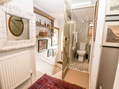 A hallway with a staircase and an open door to a small tiled bathroom at Benfield in Stow-on-the-Wold