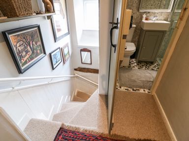 A carpeted staircase with framed pictures on the wall and a doorway leading to a bathroom with a sink and toilet at Benfield in Stow-on-the-Wold