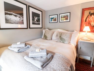 A bedroom with a bed with pillows and folded towels on it and framed artwork on the walls with a bedside table and lamp at Benfield in Stow-on-the-Wold