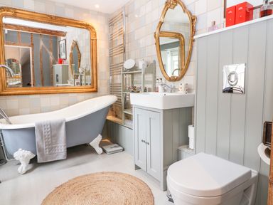 A bathroom with a freestanding bathtub a grey vanity with a sink a toilet a large gold-framed mirror and a round woven rug at Benfield in Stow-on-the-Wold