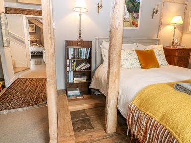 A bedroom with a bed a yellow blanket a wooden bookshelf and a lamp at Benfield in Stow-on-the-Wold