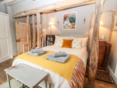 A bedroom with a bed with folded towels on a yellow throw and wooden beams at Benfield in Stow-on-the-Wold