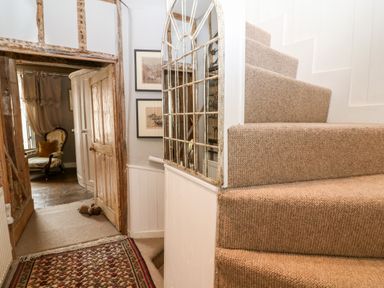 A stairway with beige carpet next to a hallway with wooden door and framed pictures on the wall at Benfield in Stow-on-the-Wold
