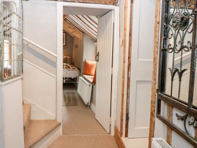 A hallway with stairs leading up and an open door showing a bed and window seat with cushions at Benfield in Stow-on-the-Wold