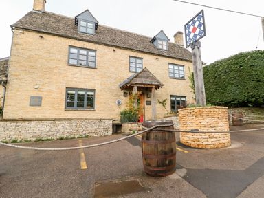 An outdoor view of a stone building with a wooden door and windows with grey frames at Anvil Cottage in Chipping Norton
