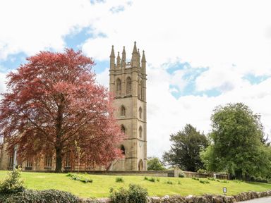 A church tower with a clock and trees on a grassy area at Anvil Cottage in Chipping Norton