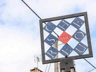 An outdoor metal sign with letters spelling service queue and a red diamond with the word the on a pole with wires and a chimney in the background