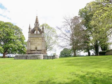 A stone monument on a grassy area with trees in the background at Anvil Cottage in Chipping Norton