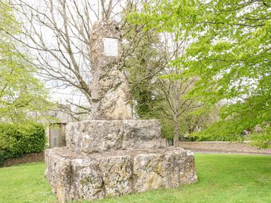 A stone monument with a plaque surrounded by trees and grass near a stone wall