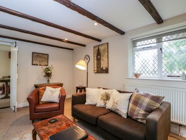 A living room with a brown sofa and armchair a wooden coffee table and a window with lattice design at Anvil Cottage in Chipping Norton