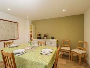 A dining room with a table set with plates and glasses a polka dot tablecloth wooden chairs a white sideboard and a large map on the wall at Anvil Cottage in Chipping Norton