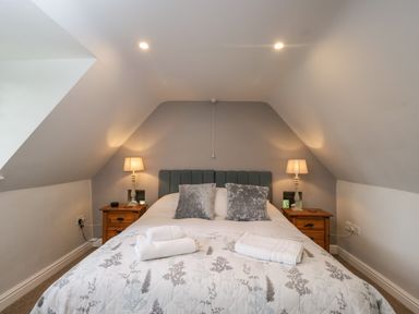 A bedroom with a bed with pillows and folded towels and two bedside tables with lamps at Anvil Cottage in Chipping Norton