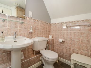 A bathroom with a white pedestal sink a toilet pink tiled walls and a small white table at Anvil Cottage in Chipping Norton