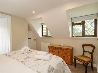 A bedroom with a bed with folded towels a wooden dresser two windows and a wooden chair at Anvil Cottage in Chipping Norton