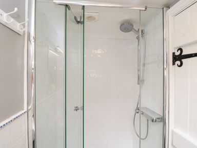 A shower enclosure with glass doors a showerhead and a white tiled wall at Anvil Cottage in Chipping Norton