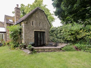 A stone cottage with a chimney and patio furniture in a garden with plants and grass at Anvil Cottage in Chipping Norton