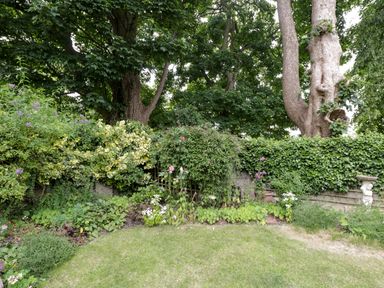A garden with grass lawn flowers shrubs trees and a birdbath at Anvil Cottage in Chipping Norton