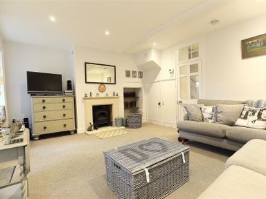 A living room with a sofa a chest of drawers a TV fireplace and a wicker coffee table at Hare House in Chipping Norton
