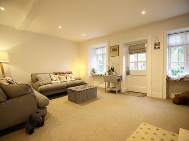 A living room with sofas cushions a wicker coffee table a lamp and windows with seating at Hare House in Chipping Norton