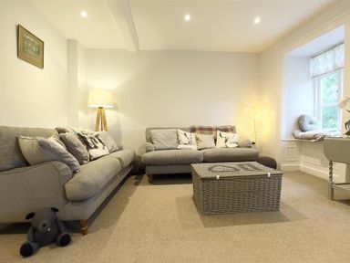 A living room with two grey sofas a wicker coffee table a table lamp and a window seat at Hare House in Chipping Norton
