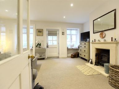 A sitting room with a fireplace a mirror above it a chest of drawers and a window seat at Hare House in Chipping Norton