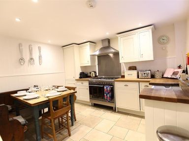 A kitchen with a dining table set with plates and glasses and white cabinets at Hare House in Chipping Norton